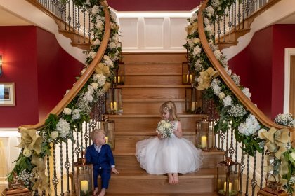 Flower girl and page boy sitting on stairs decorated with flower garland