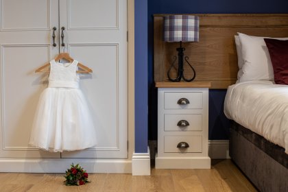 Bedroom showing flower girl dress on hanger with bouquets of flowers on wooden floor underneath