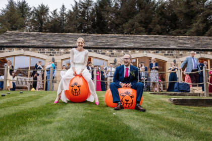 Bride and groom bouncing on space hoppers on grass